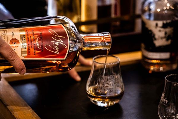 A hand pours amber whiskey from a bottle into a glass on a bar counter.