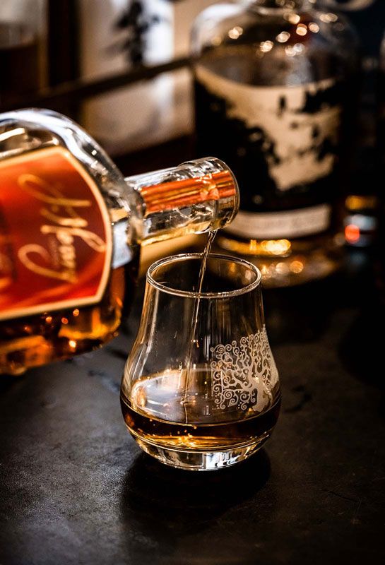 Amber liquor being poured into a glass on a dark bar counter