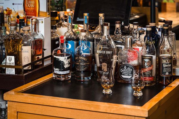 Assorted liquor bottles and glasses displayed on a wooden bar counter with a mirrored back shelf