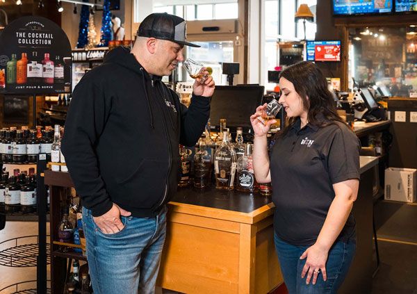 Two people tasting drinks at a bar counter, with bottles and taps in the background.