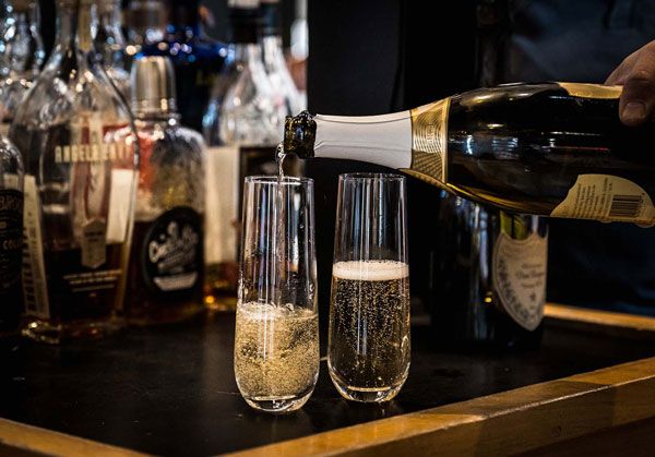 Champagne being poured into a flute beside a half-filled glass at a bar counter