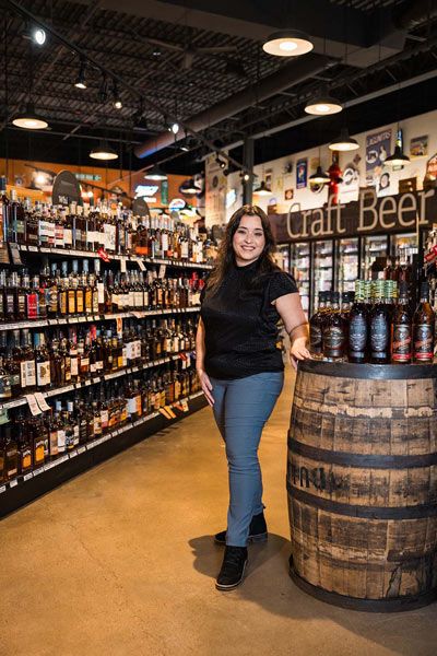 Woman standing in a craft beer store beside a large wooden barrel display