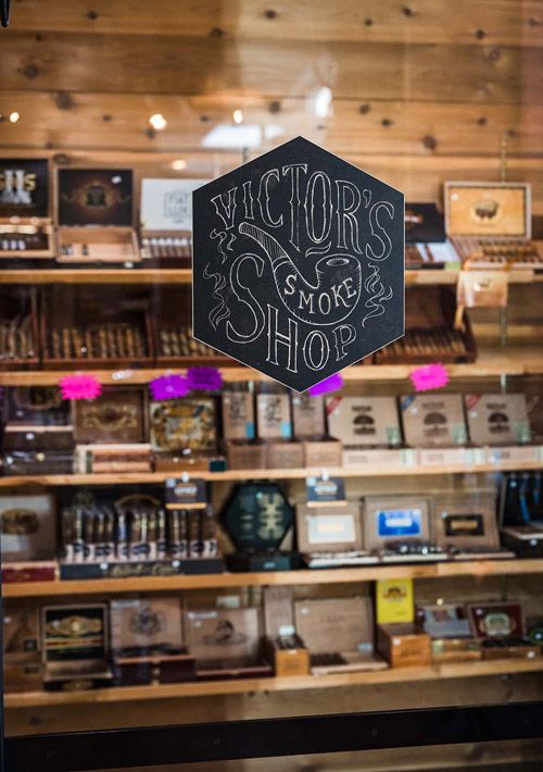 Interior of a cigar shop with wooden shelves, boxes, and a large “Victors” sign on the wall.