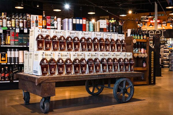 Display of brown liquor bottles on a wooden cart inside a well-lit store