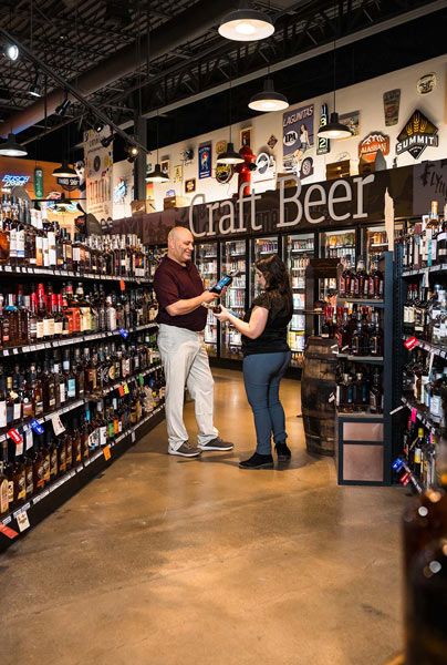 Two people chatting in a craft beer store aisle, surrounded by rows of bottles.