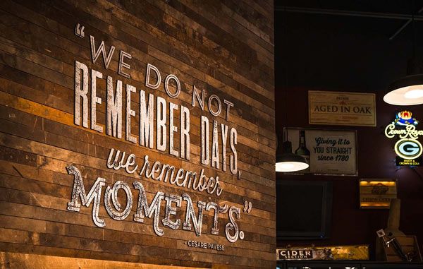 Wooden wall sign reading “We do not remember days, we remember moments” in a dimly lit bar interior
