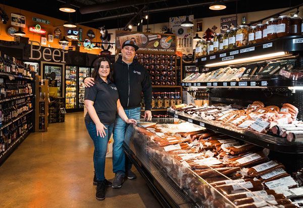 Two people standing in a grocery store aisle beside a refrigerated meat display