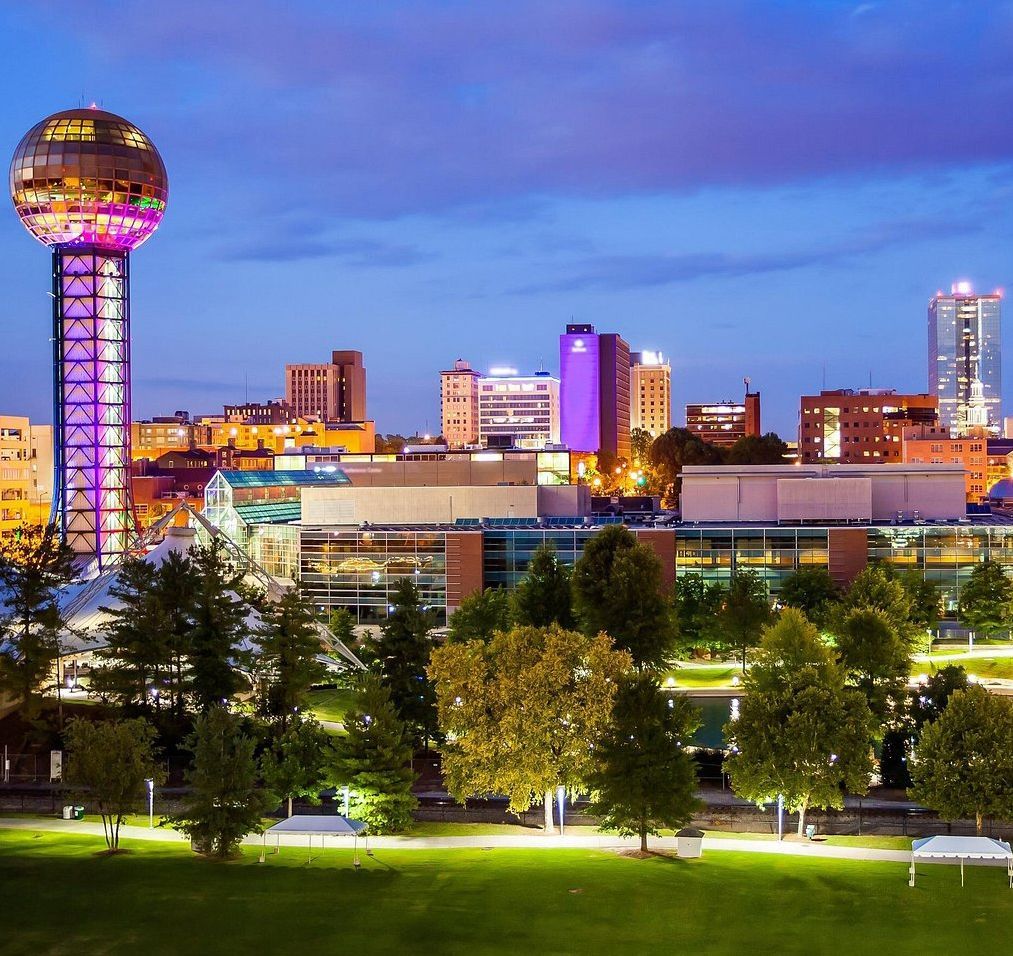 Knoxville, TN skyline at dusk with the Sunsphere lit up and a park in the foreground.