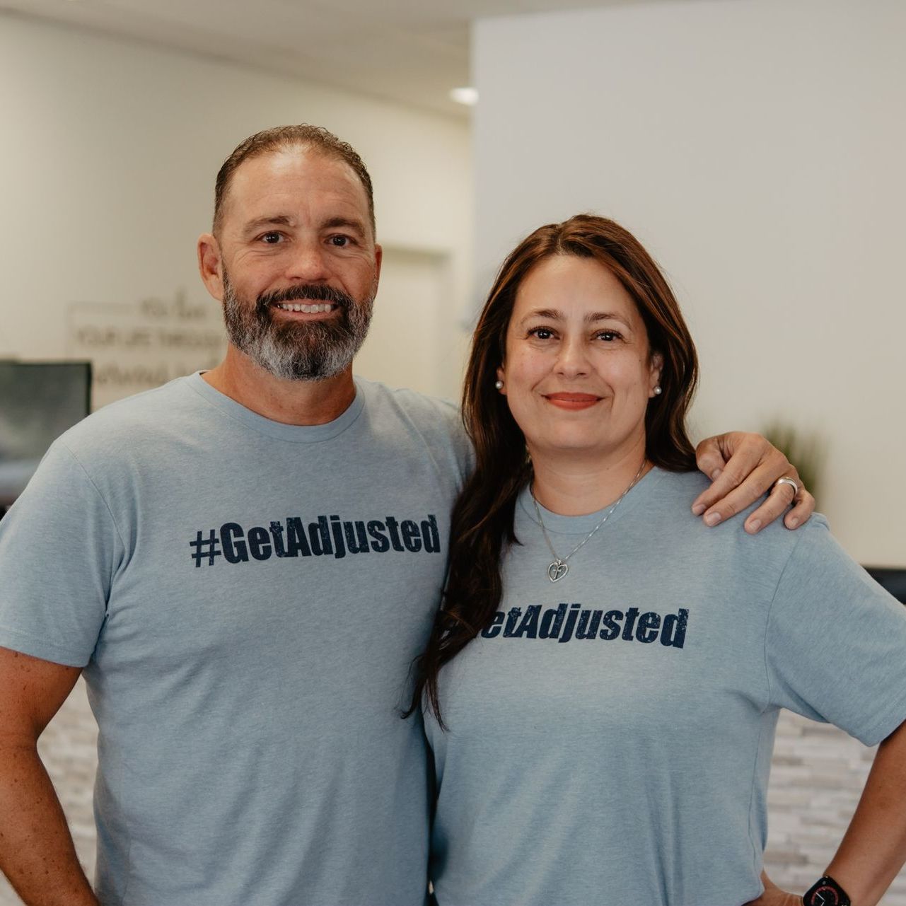 A man and a woman are posing for a picture while wearing #getadjusted shirts