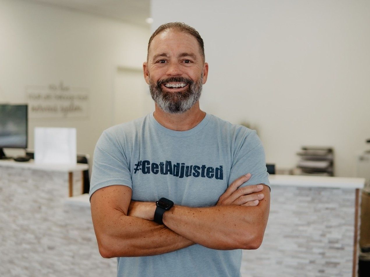 A man with a beard is wearing a t-shirt that says get adjusted.