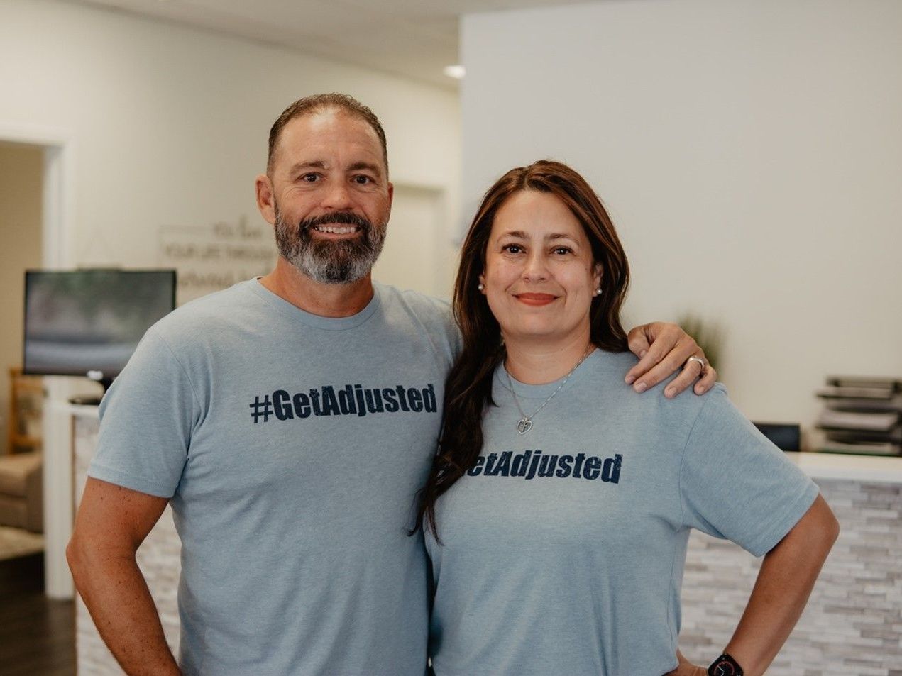 A man and a woman are posing for a picture while wearing t-shirts that say get adjusted.