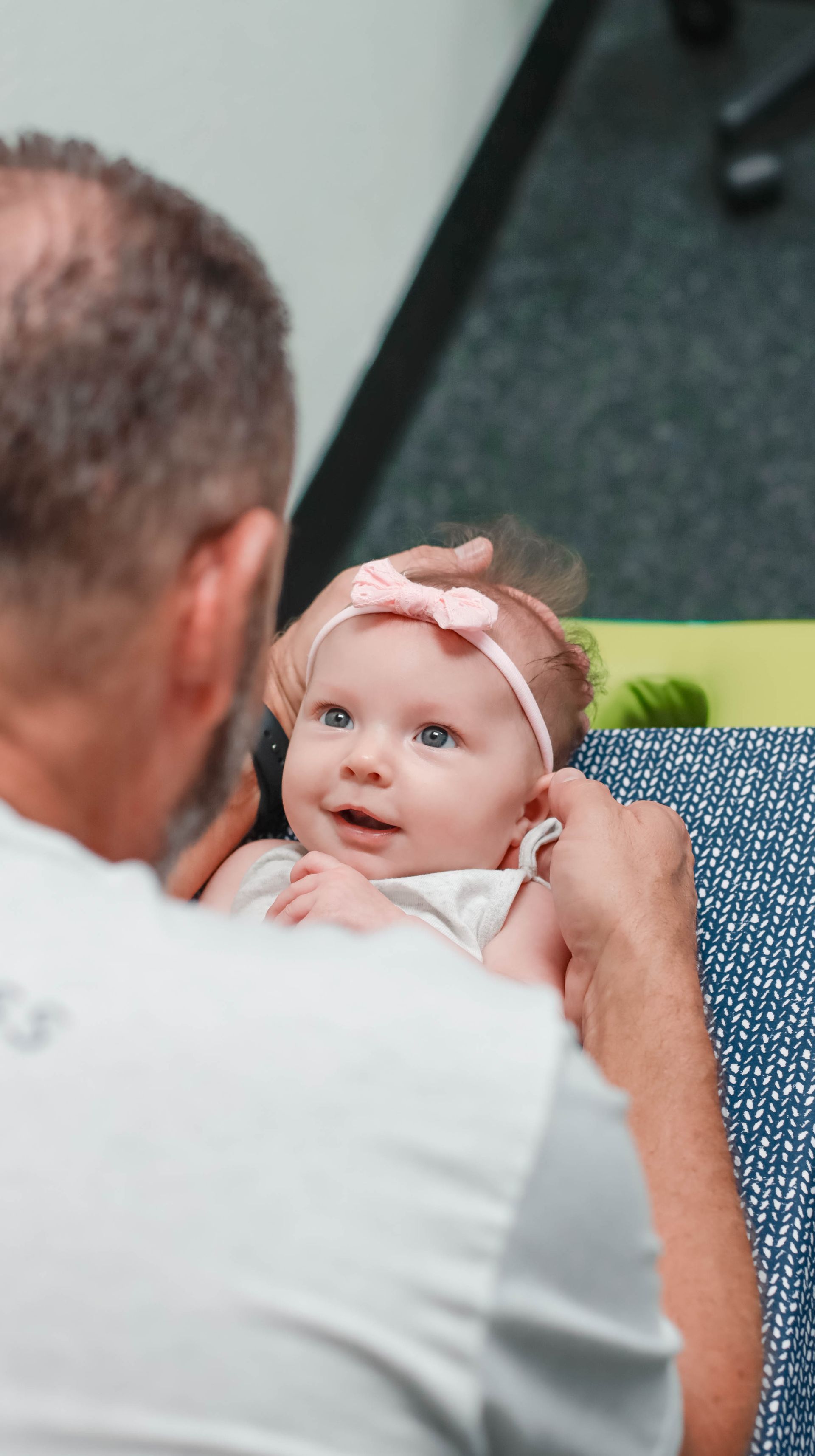 A man is holding a baby girl with a pink headband on her head.
