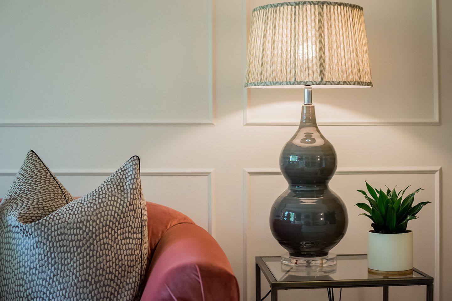 Pink sofa with a taupe cushion. Grey table lamp on glass table. Wall panelling in F&B Dimity