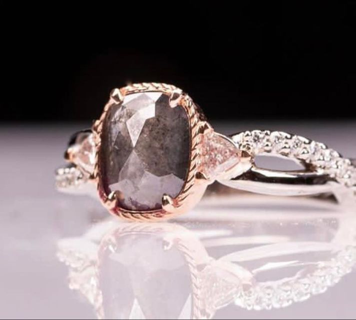 Rose gold ring with oval dark gemstone and small clear side stones on a reflective surface