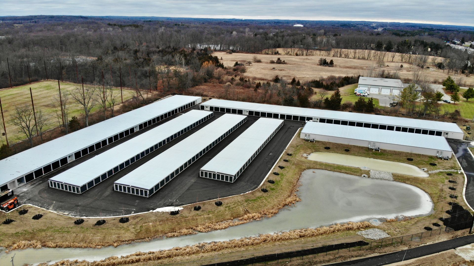 Aerial view of a large white-roofed storage facility with long rows of units and surrounding fields