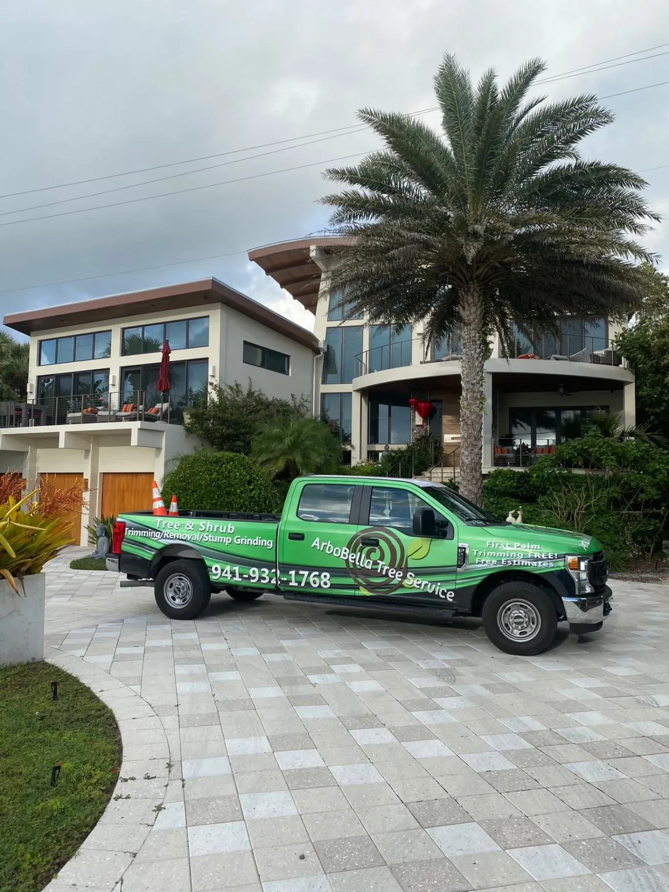 Green pickup truck parked in front of a modern house with palm trees and a tiled driveway