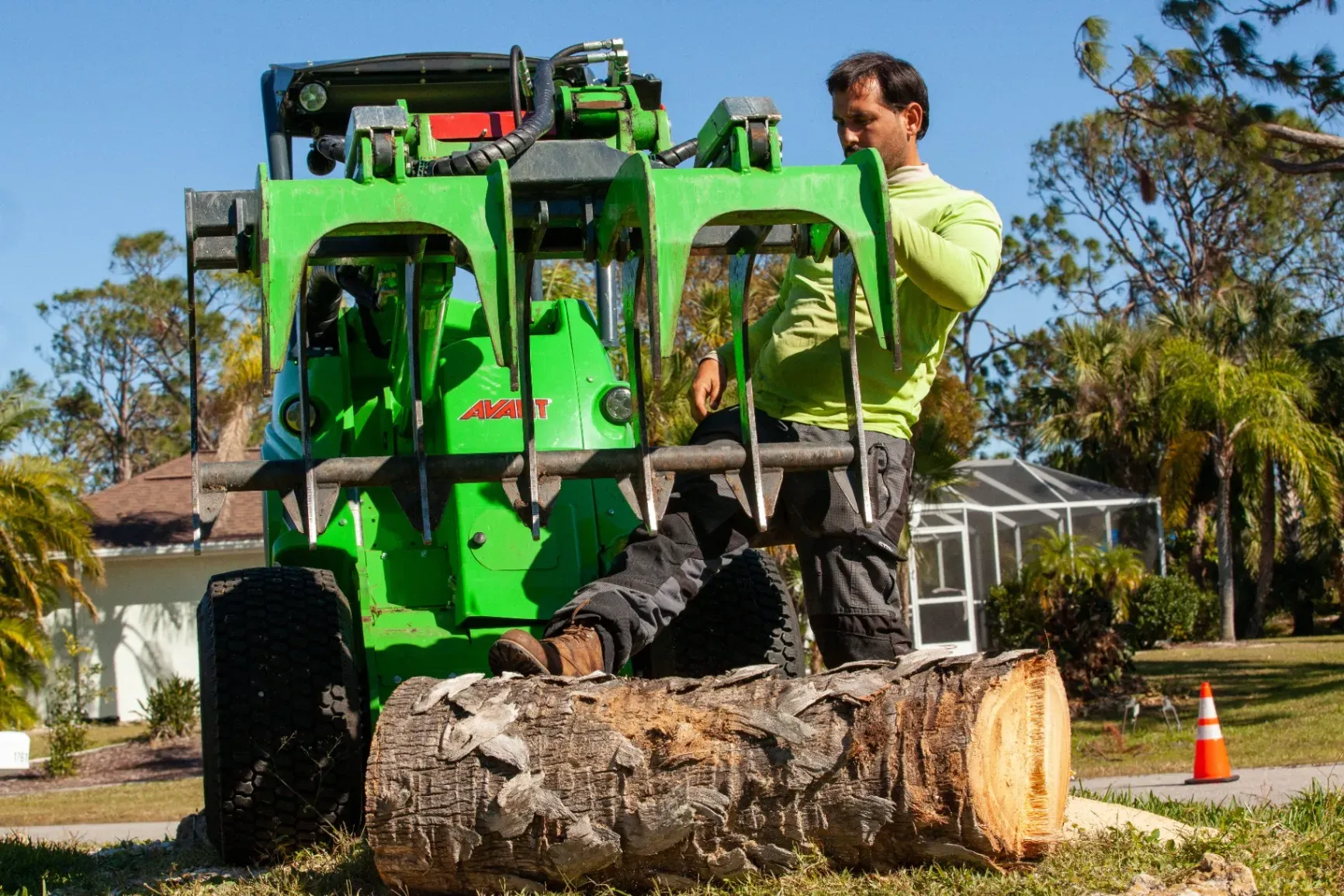 Worker on a green wood chipper cuts a large log on a suburban street.