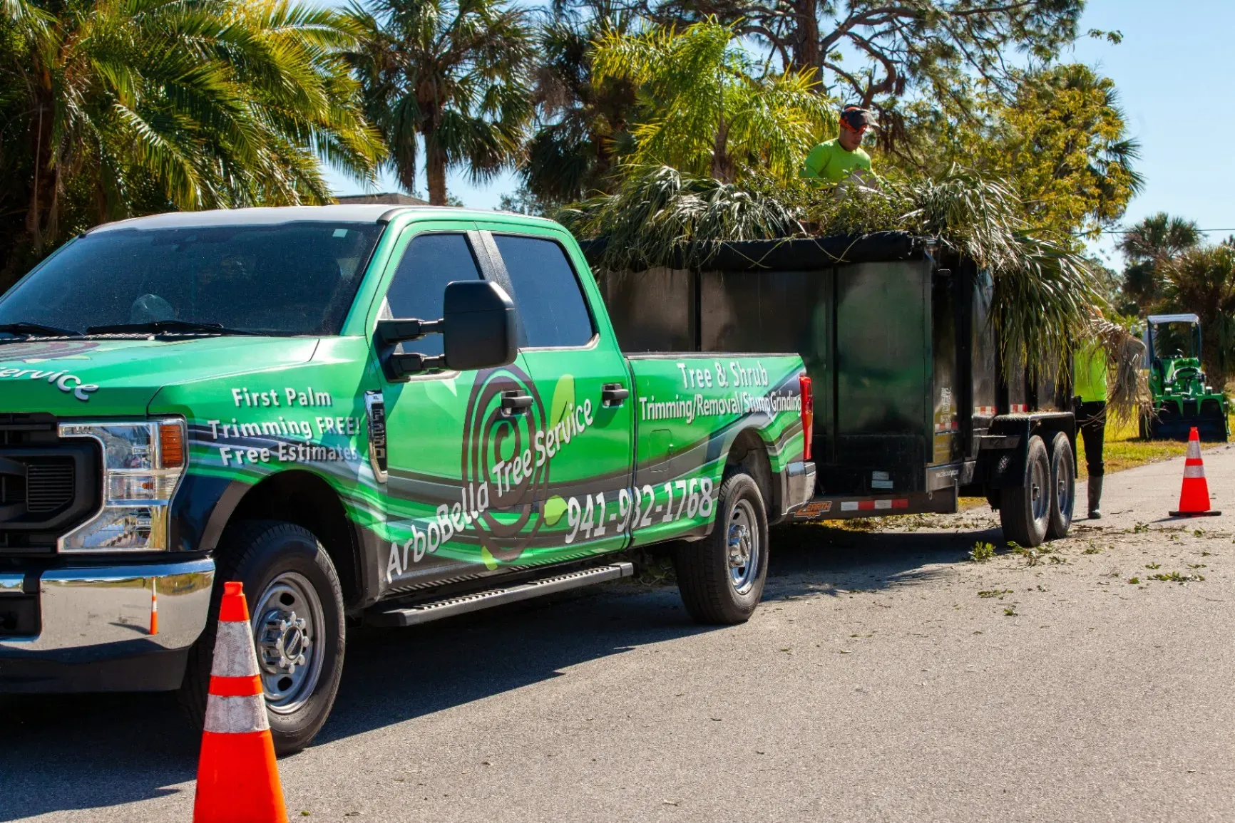 Green pickup truck parked roadside with orange cones and a trailer in the background