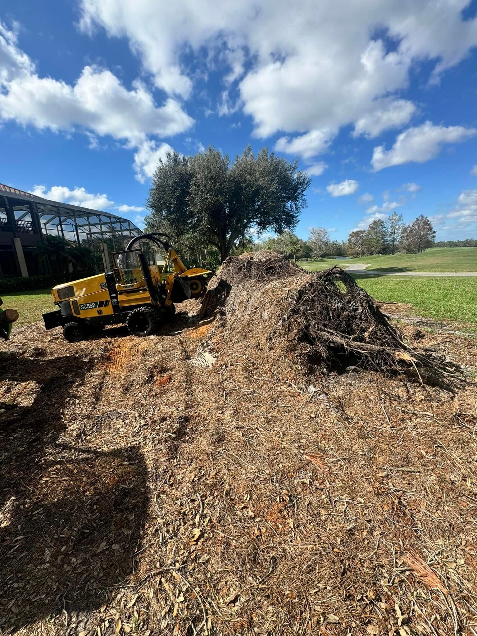 Yellow excavator beside a large mulch pile in a sunny field under a blue sky