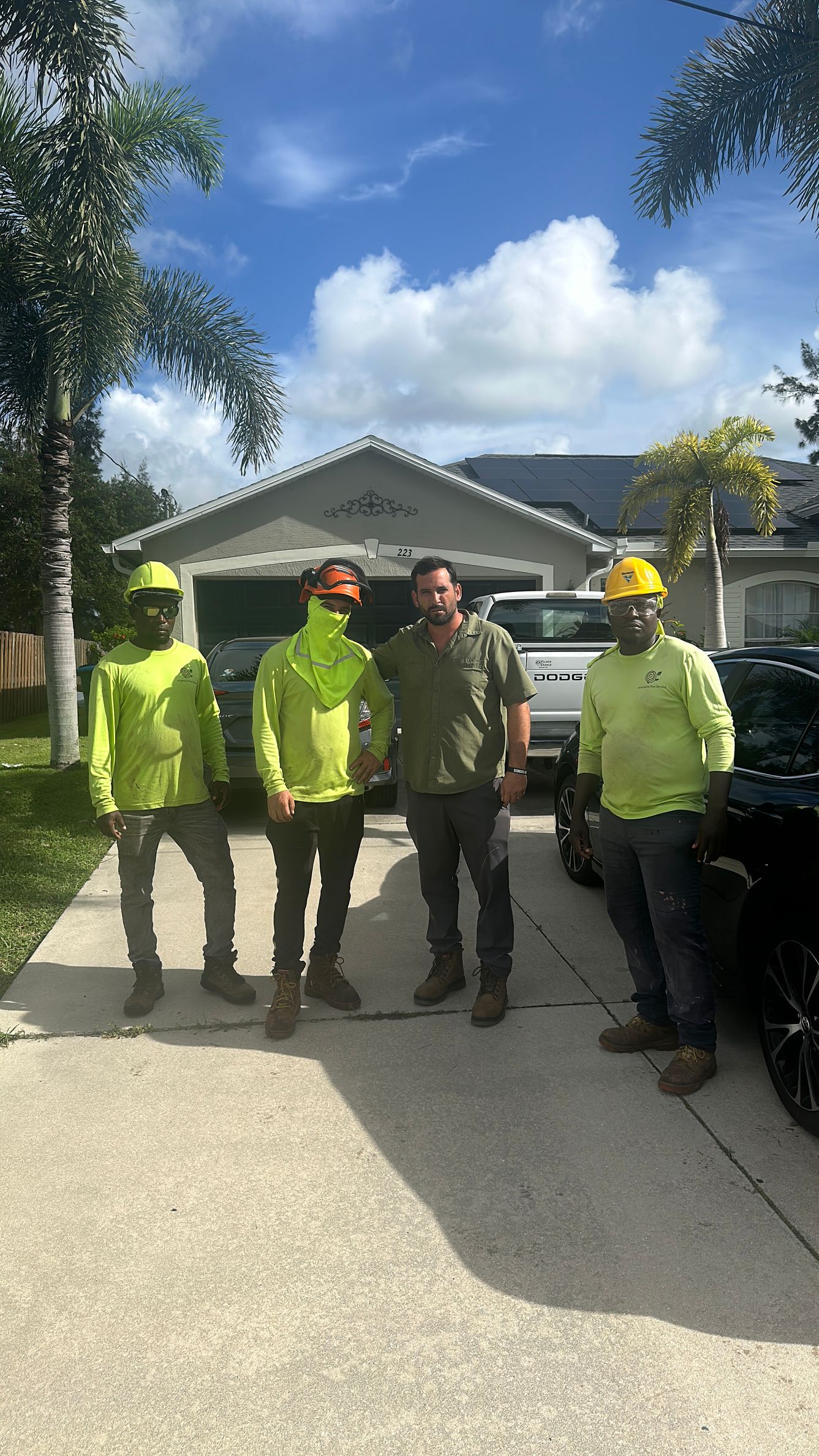 Four workers in neon safety gear stand on a driveway in front of a house on a sunny day