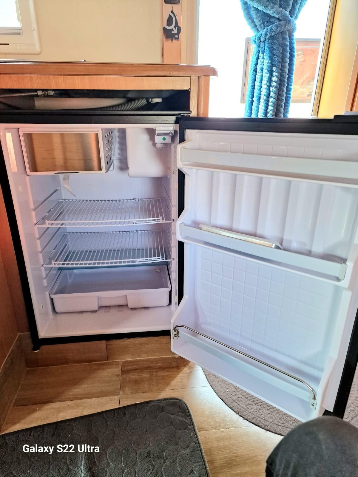 Minifrigo aperto con ripiani e spazio nella porta, in una stanza con finestra e dettagli in legno.
