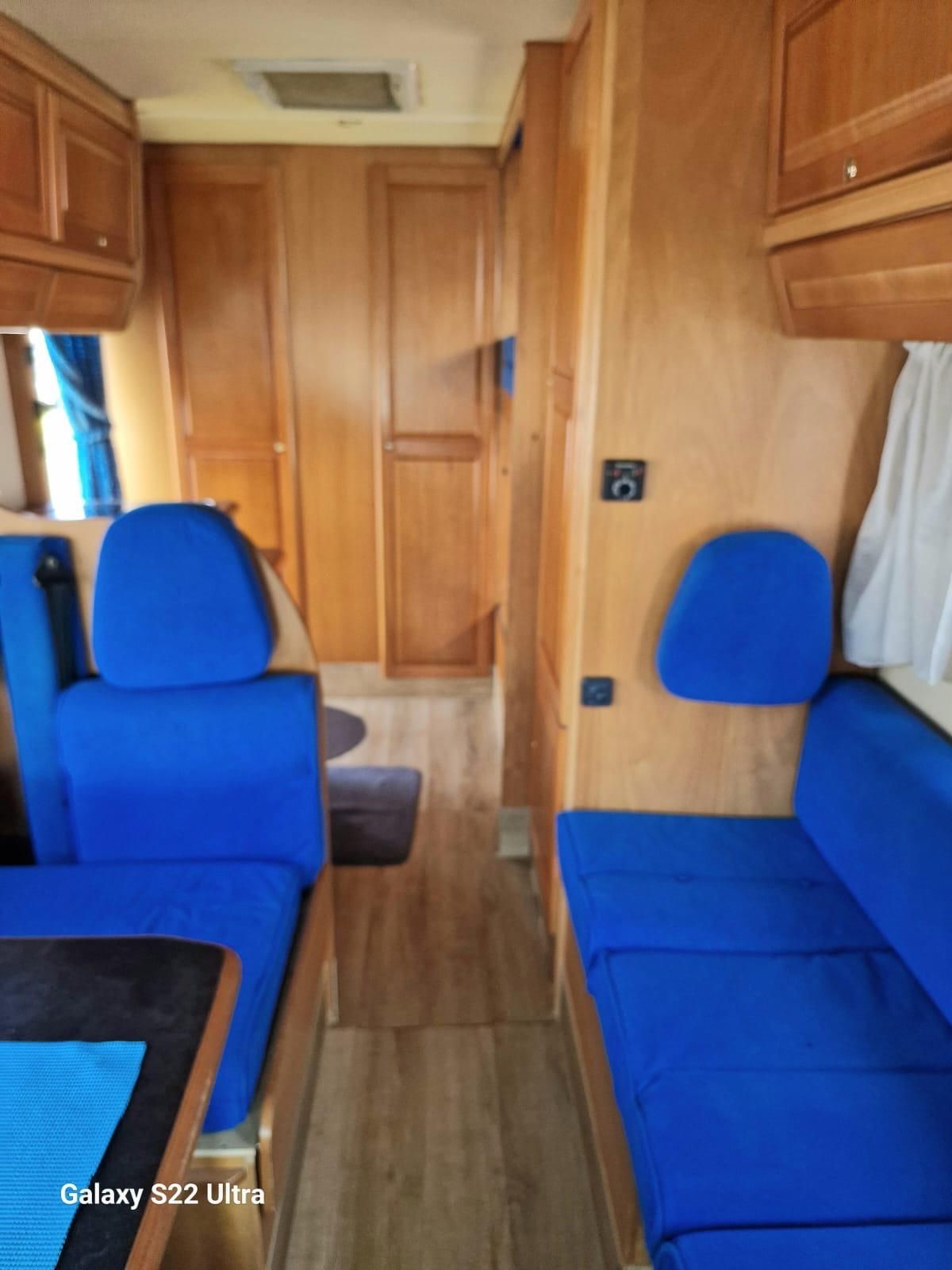 Interno di un camper con sedili blu e pannelli in legno chiaro.