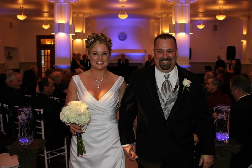 Newly married couple walking down the aisle after ceremony. Bride in white dress and groom in suit, smiling.