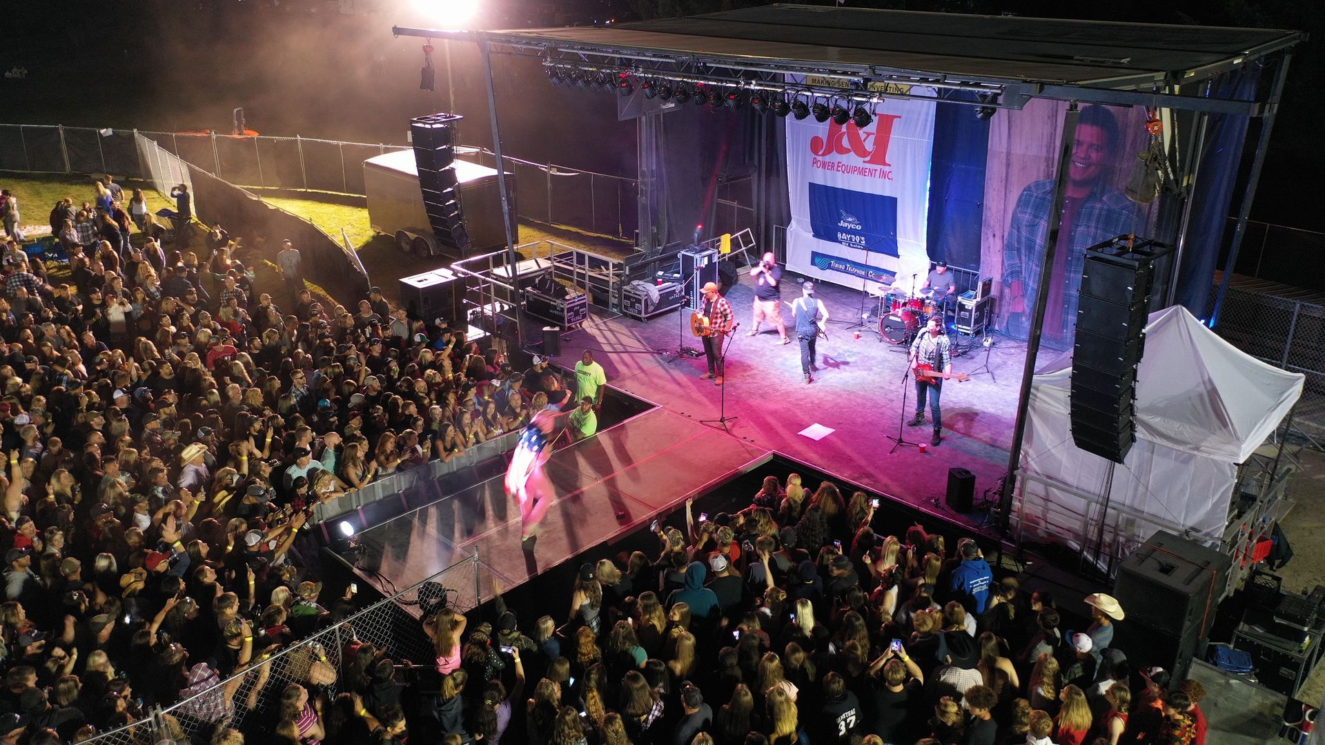A band performs on an outdoor stage at night before a large crowd. Stage has lights and a large screen.