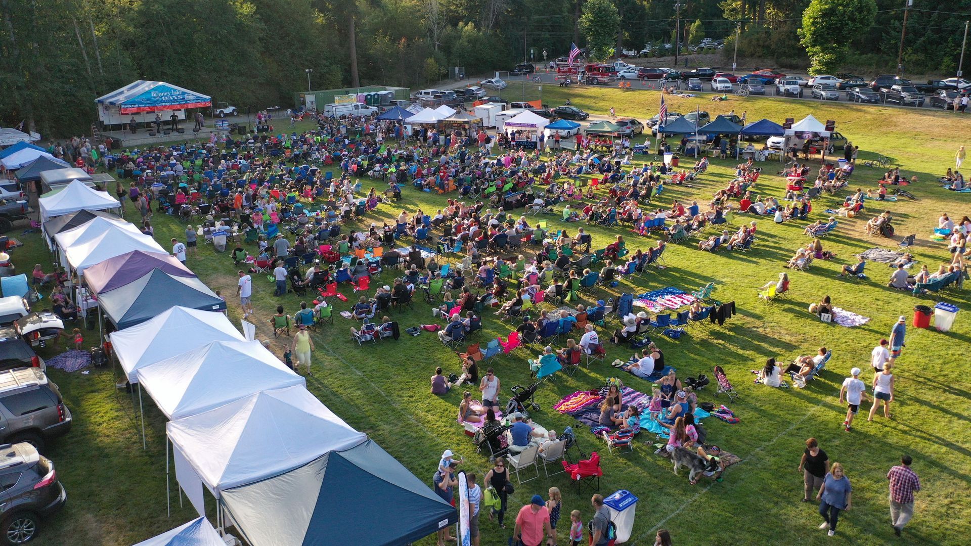 Large crowd at an outdoor event with tents and people seated on the grass.