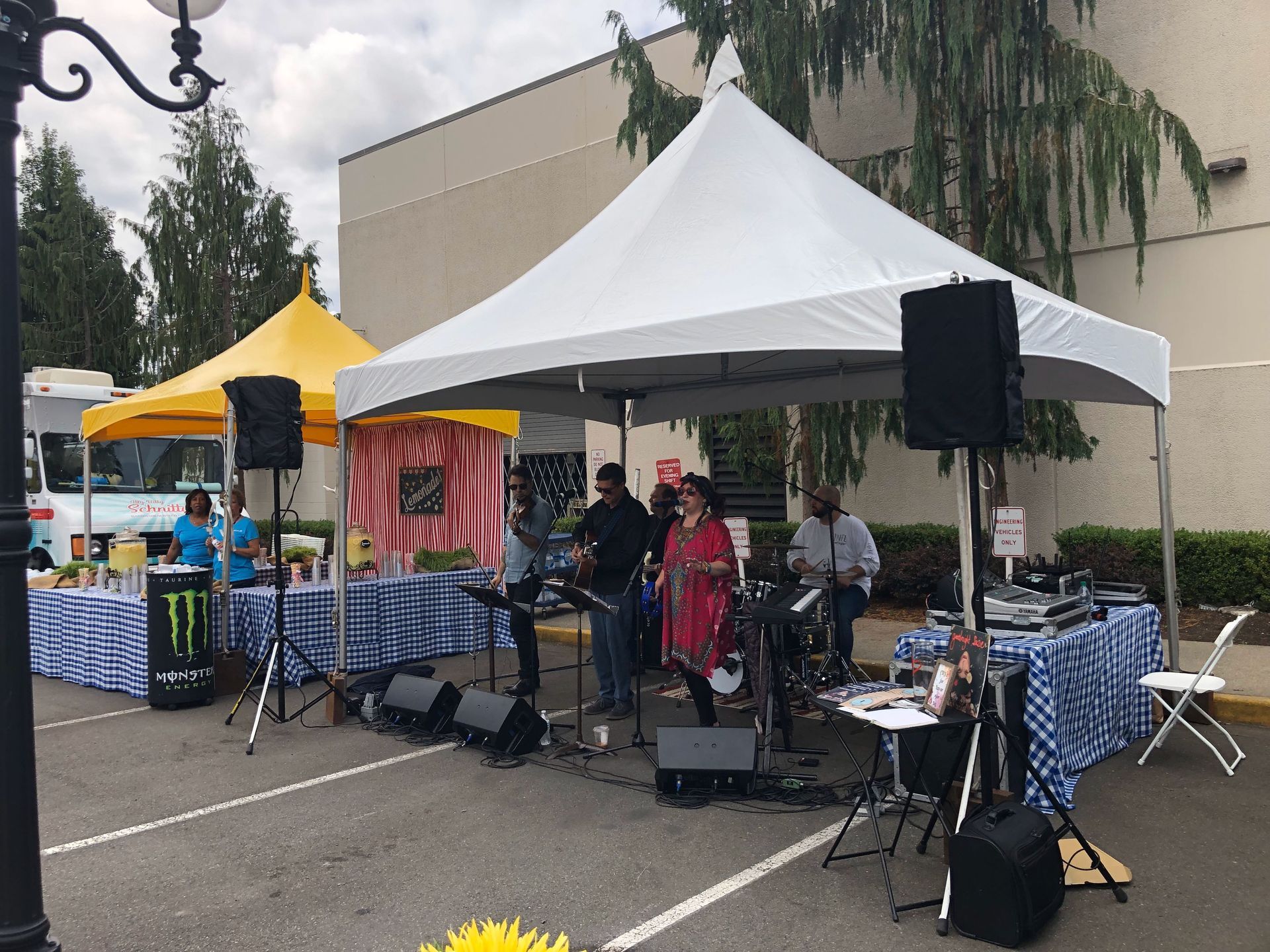 Outdoor event with a band playing under a white tent; food vendors in the background.