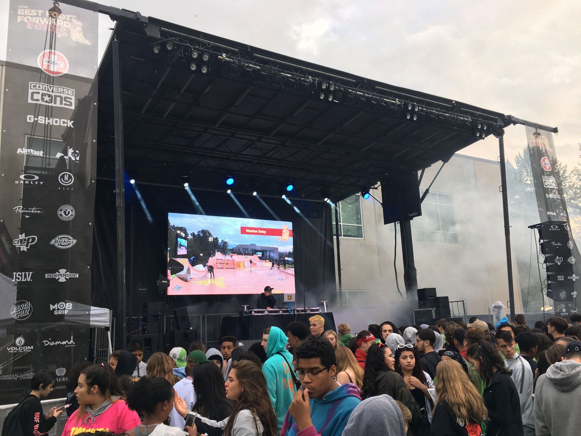 A DJ performs on a stage at an outdoor event, with a large crowd watching.