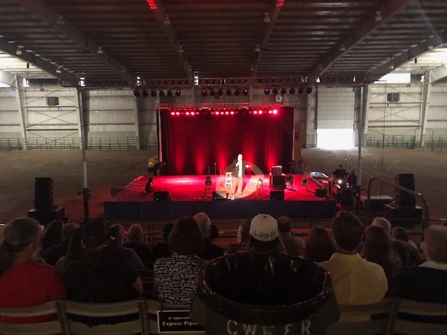Stage lit red, with a performer on stage and an audience seated. Concert hall setting.