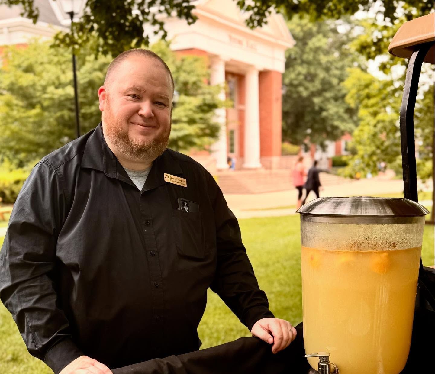 A person in a black shirt stands next to a large, full beverage dispenser.