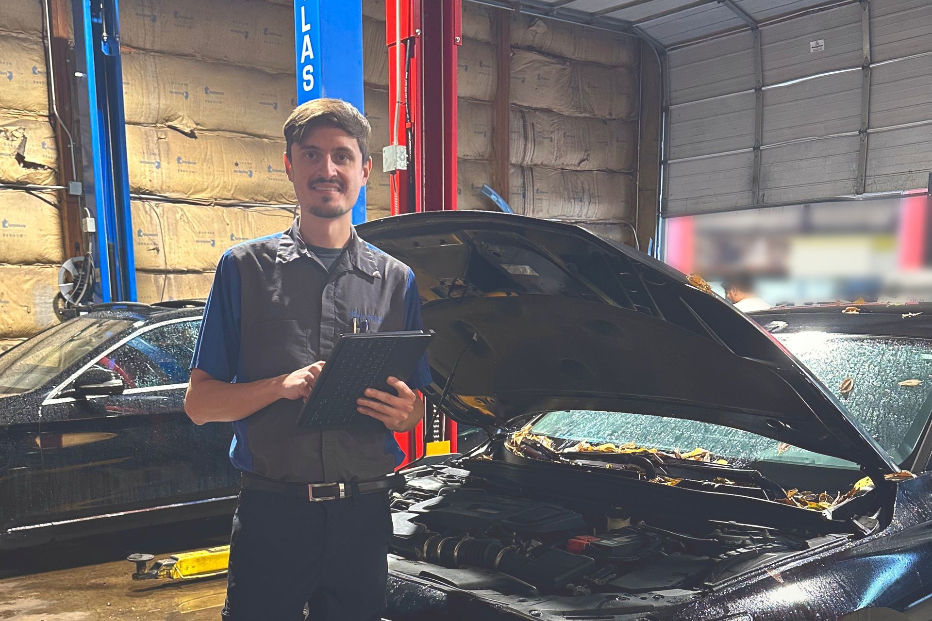 Mechanic standing beside a car with its hood open in a workshop