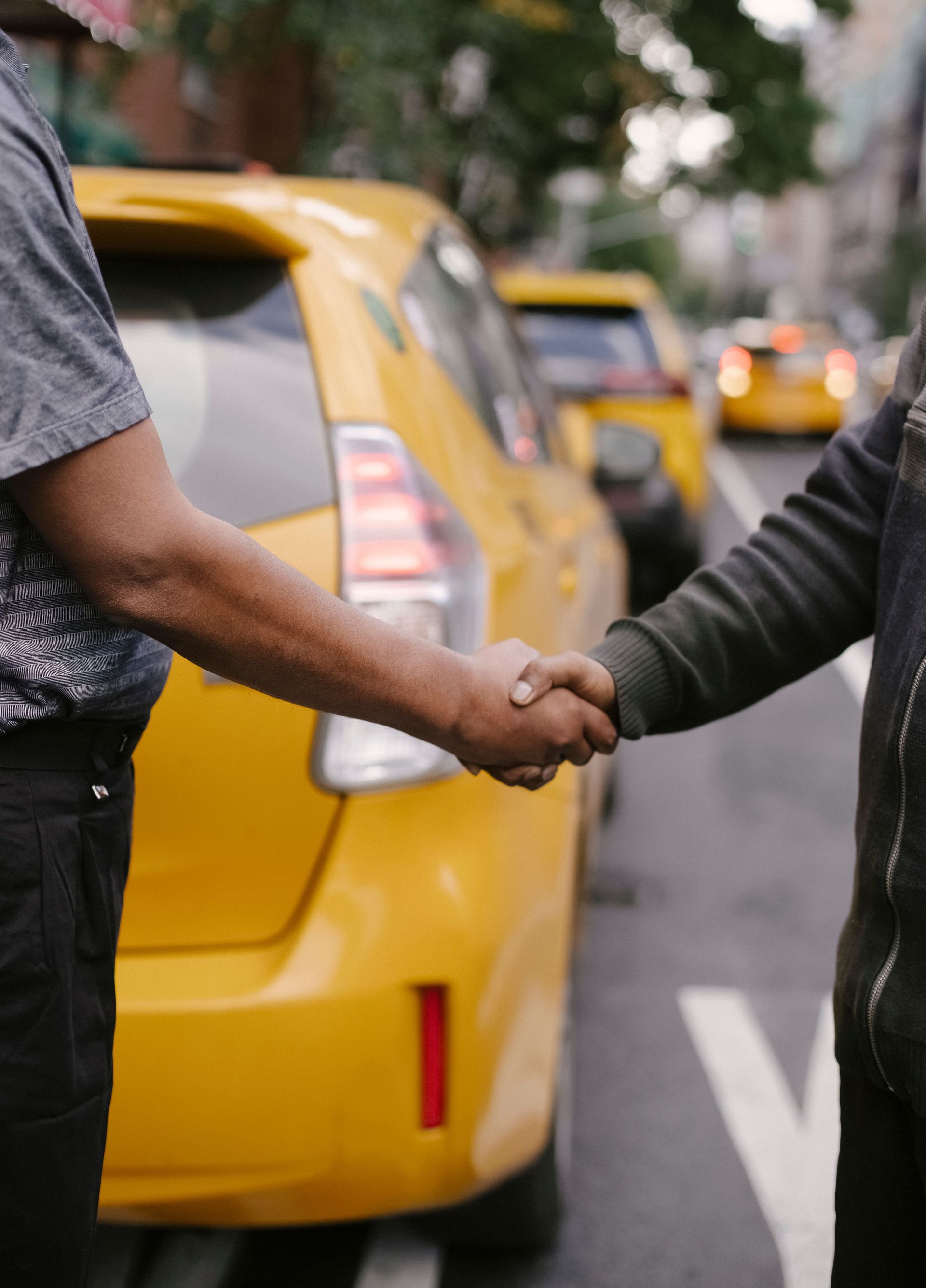 Two people shake hands beside a yellow taxi on a city street.