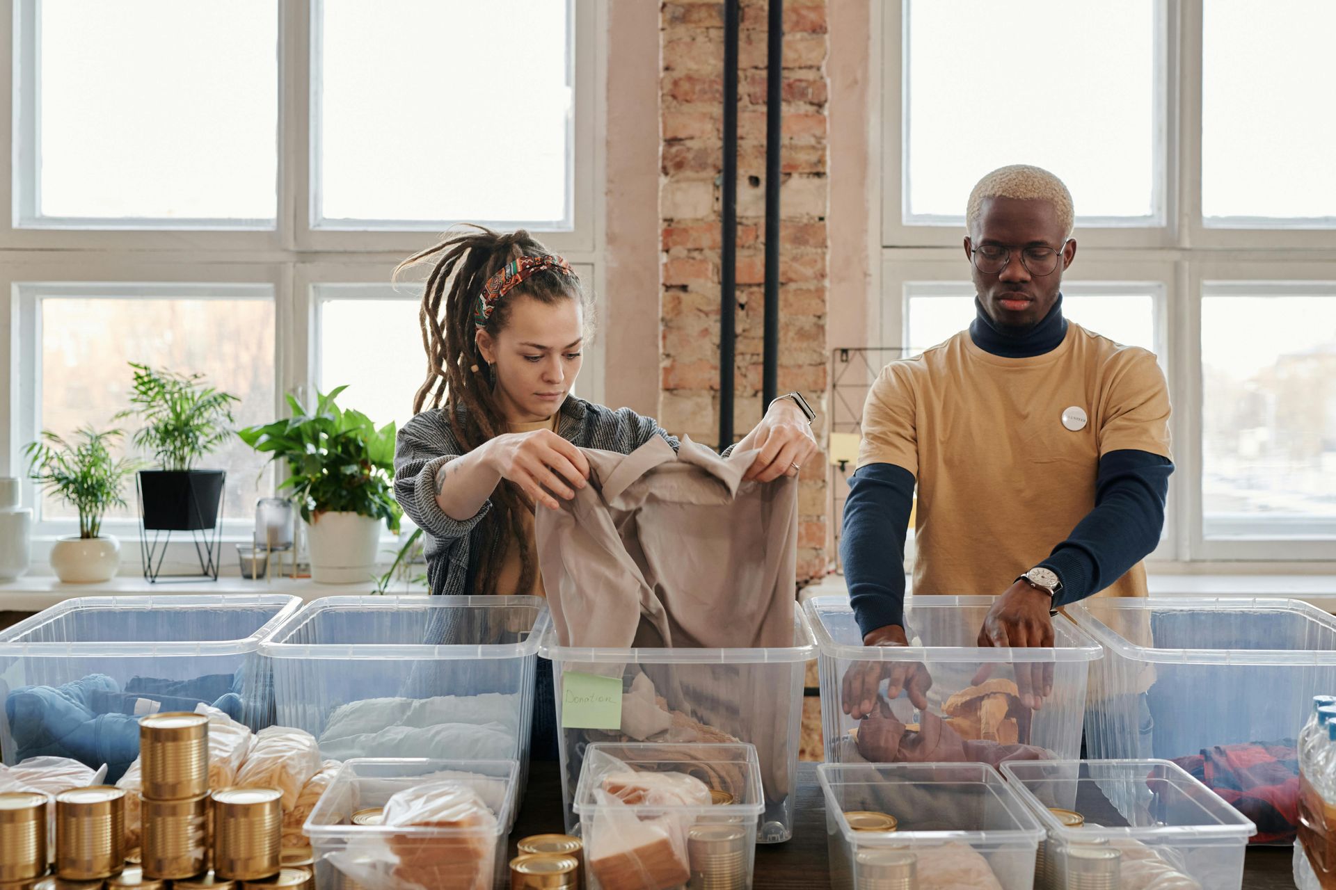 Two people sorting items into clear bins at a table indoors.