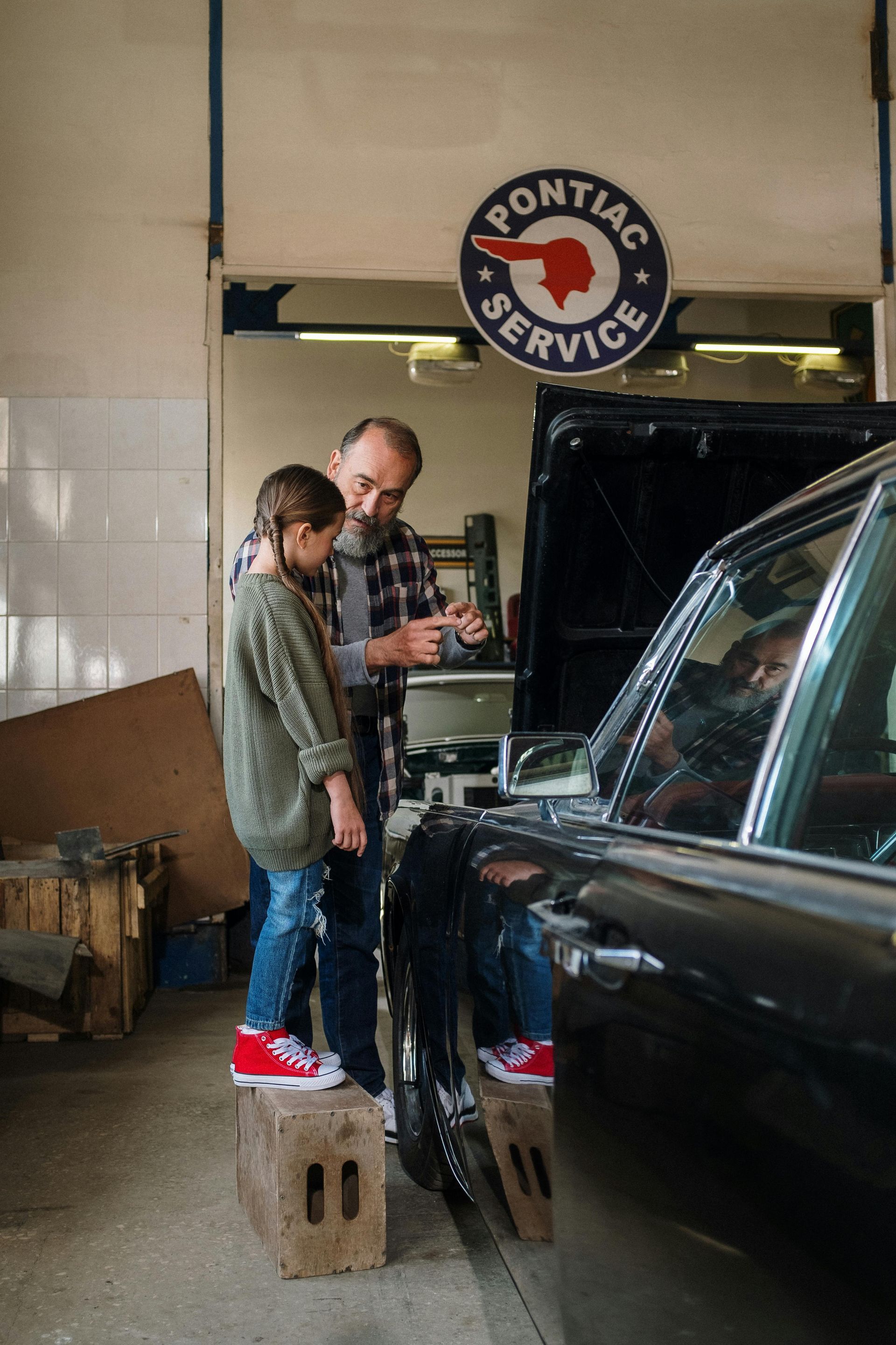 Um homem e um menino estão trabalhando em um carro em uma garagem.