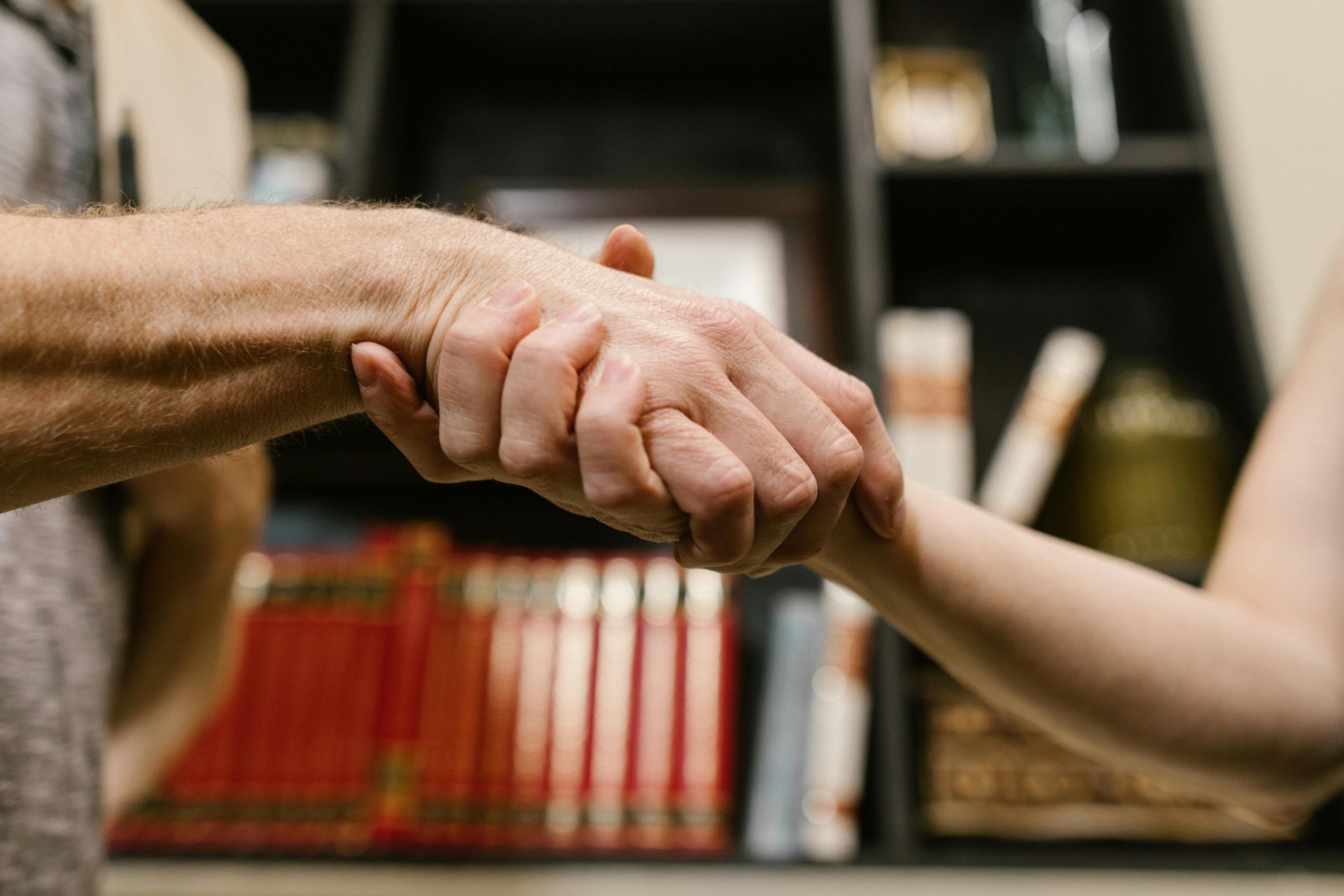Um homem e uma mulher apertam as mãos em frente a uma estante de livros.