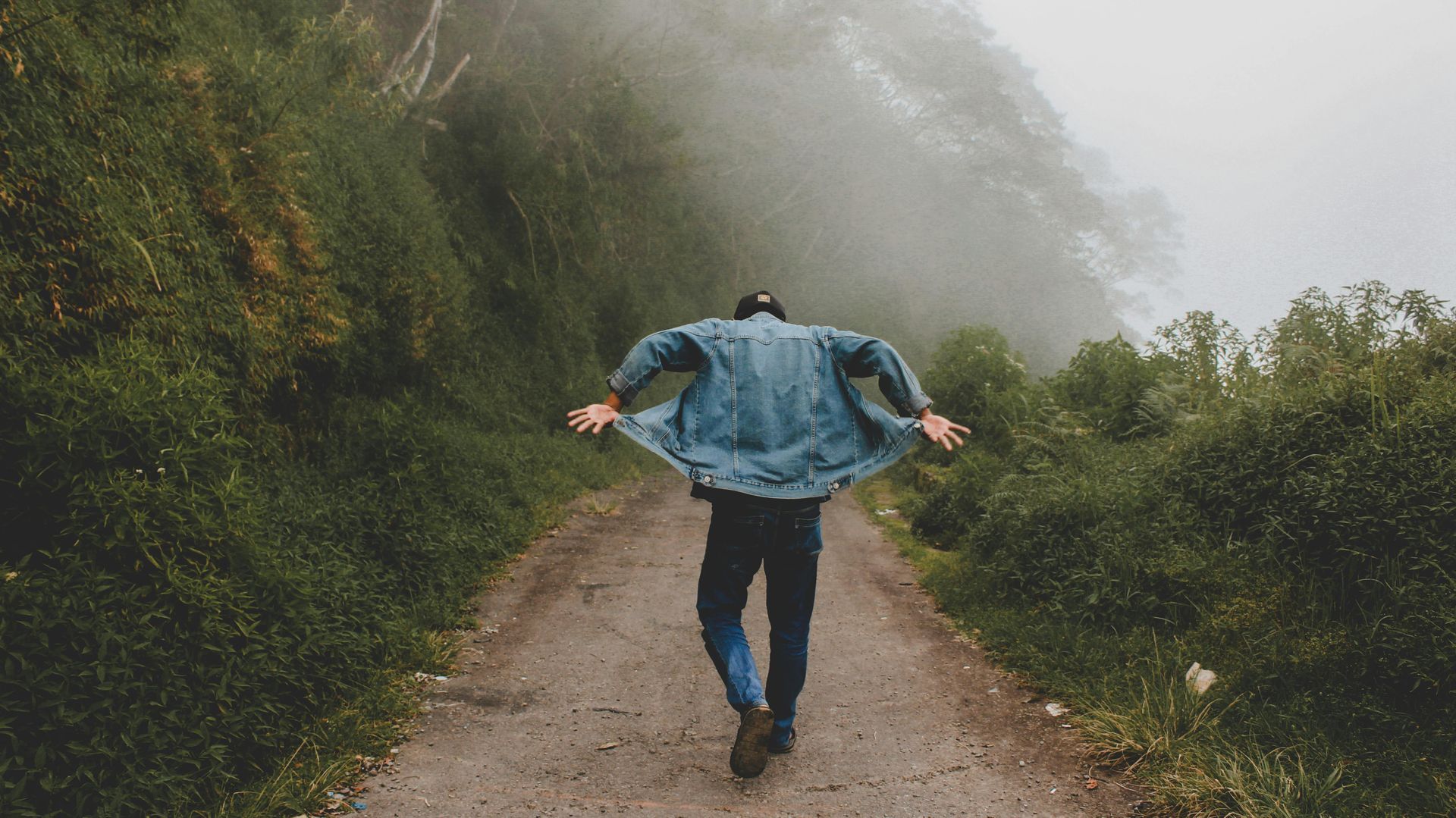 Um homem está caminhando por uma estrada de terra com os braços estendidos.