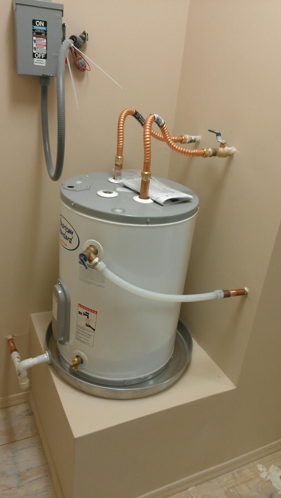 Water heater tank with copper pipes and electrical box in a utility closet.