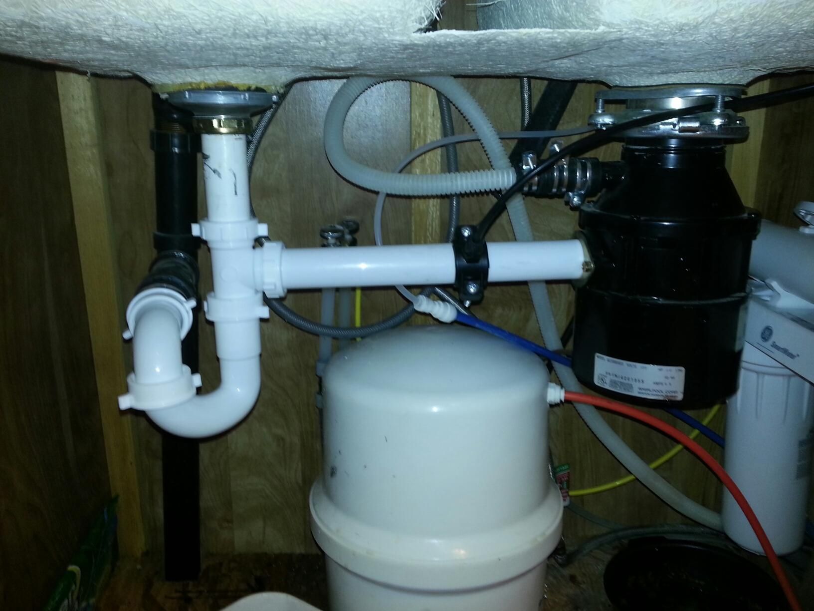 Under-sink plumbing with white pipes and a black garbage disposal