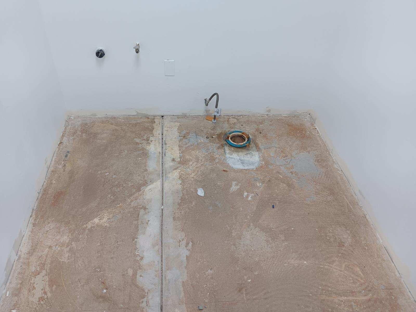 Empty room with unfinished floor, exposed pipes, and a wall outlet near the back wall