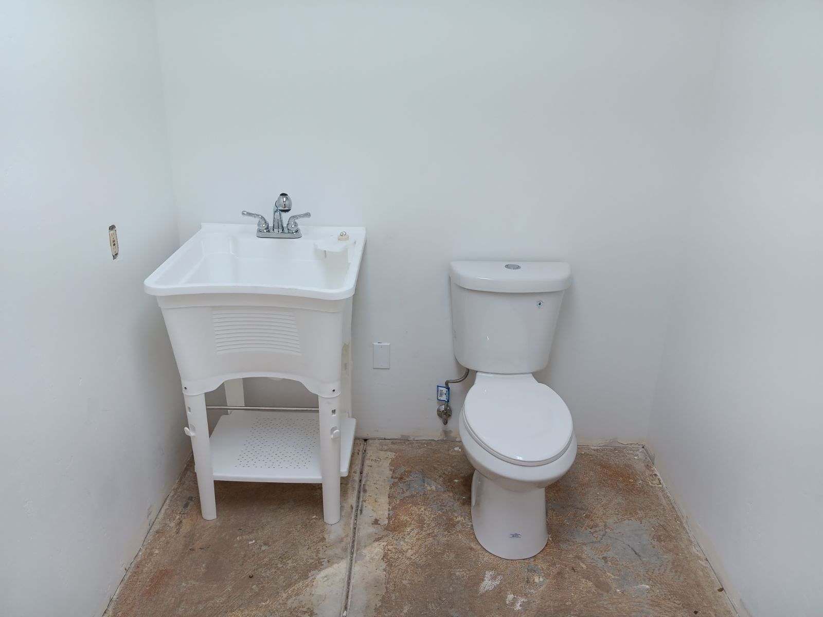 Small white bathroom with a sink on the left and a toilet on the right, on a bare concrete floor
