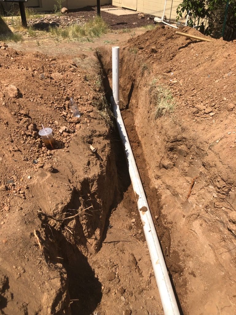 White PVC pipe laid in a dirt trench beside a dug-up yard
