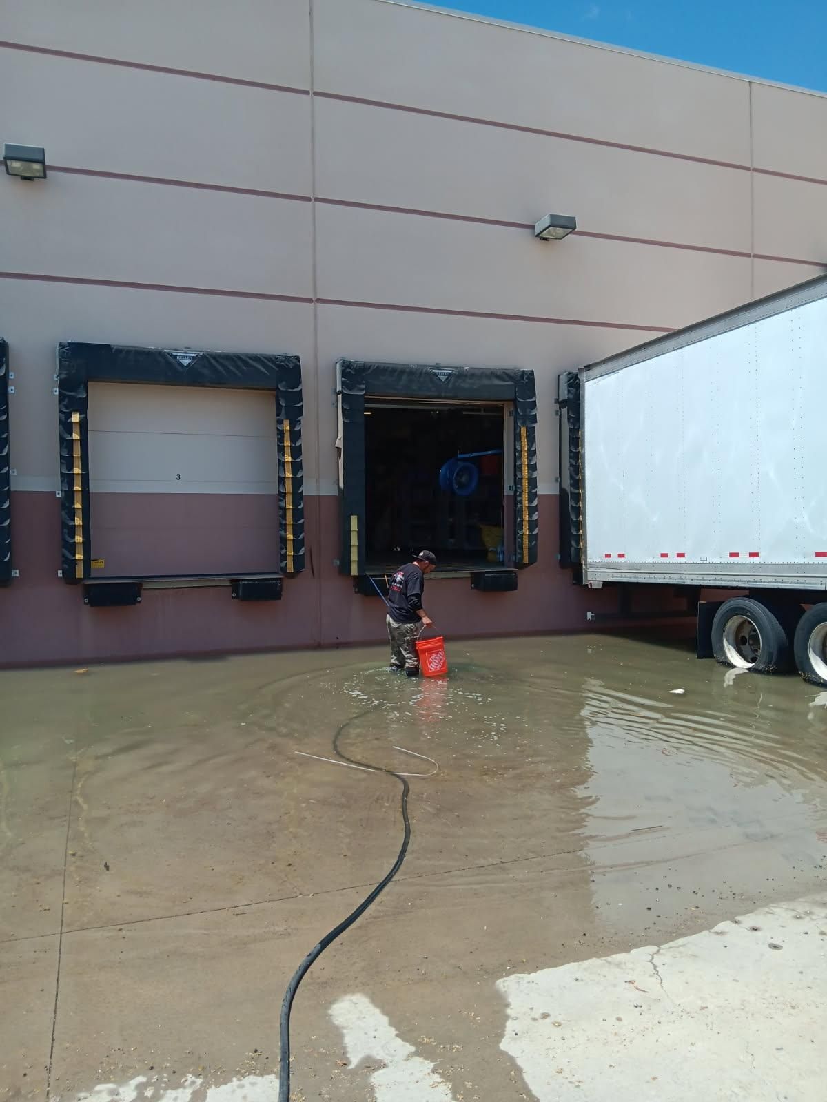 Truck loading dock with a worker spraying water on the wet pavement near a semi-trailer