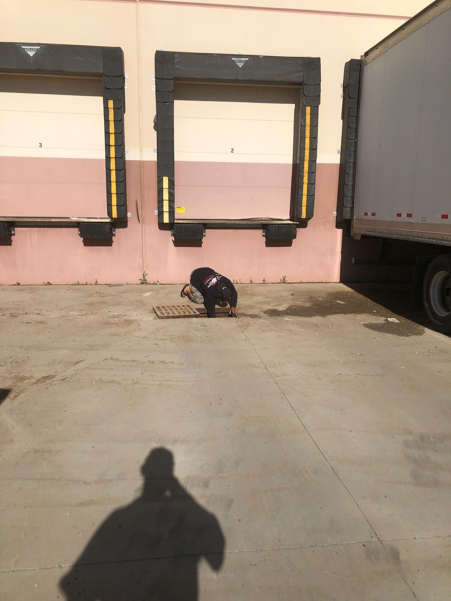 Person crouching on a sidewalk beside loading dock doors, with a truck parked on the right.