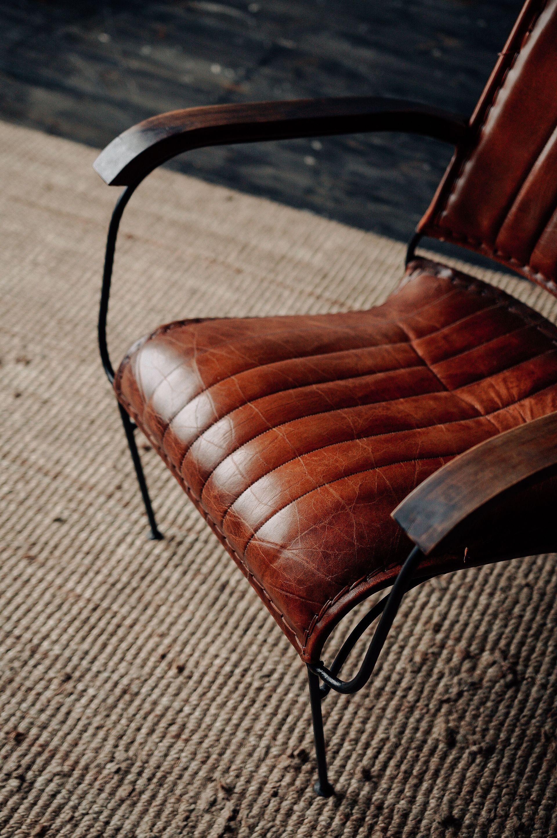 Brown leather chair with black metal arms on a beige carpet in warm light