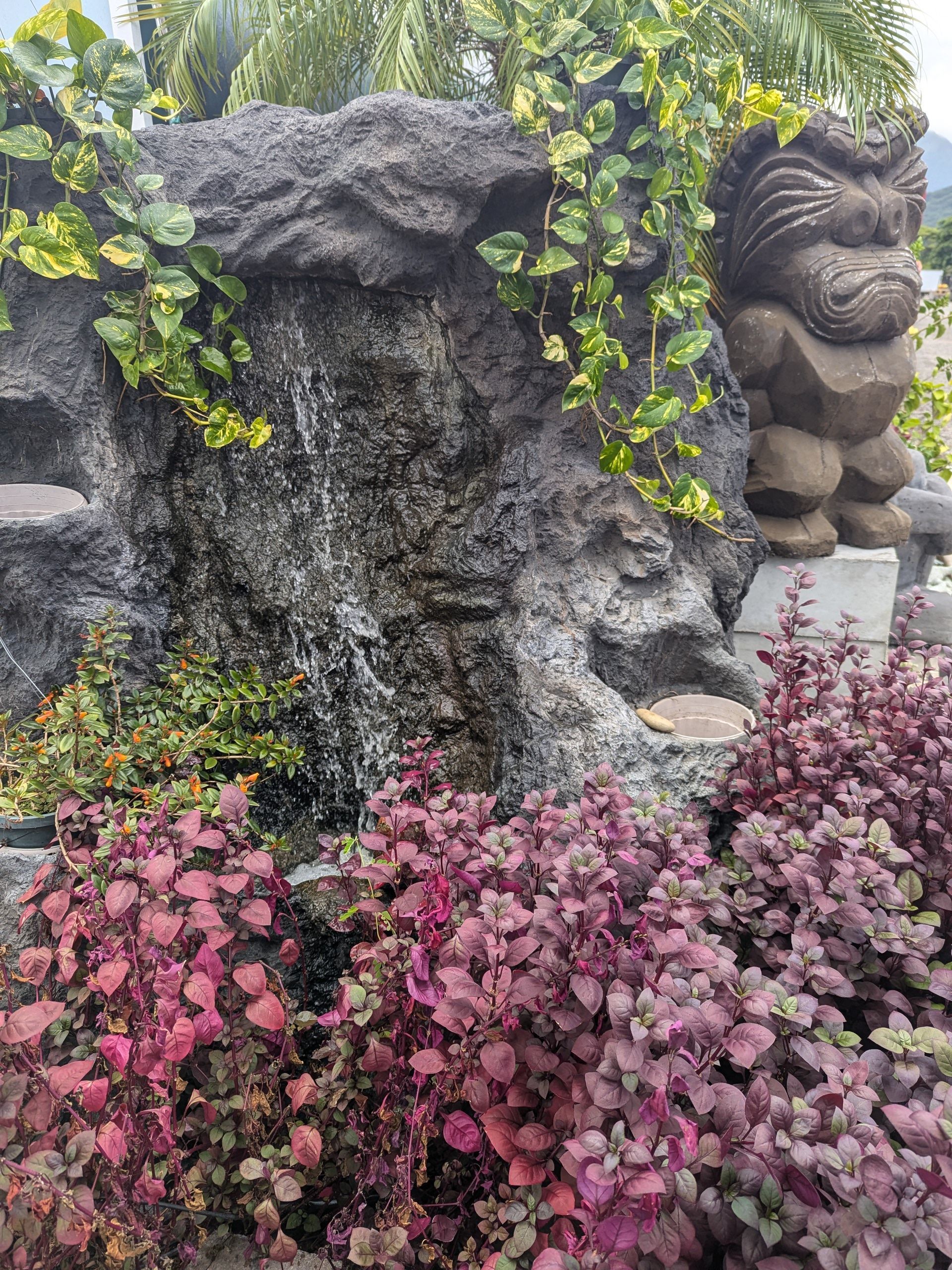 There is a statue in the middle of a garden surrounded by plants.