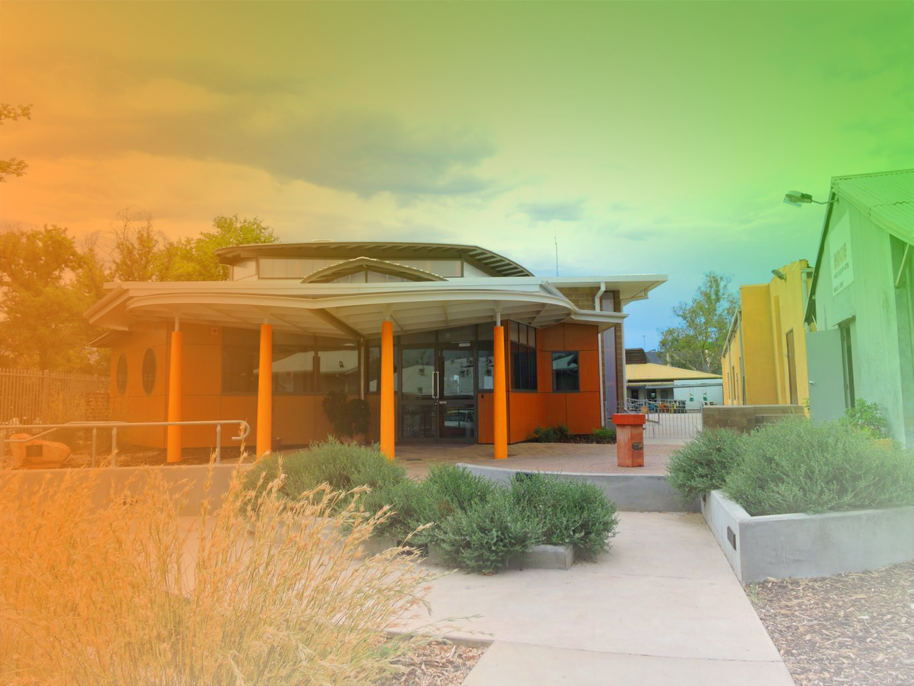 Orange building with a covered entrance and bushes in front. A path leads up to the door.