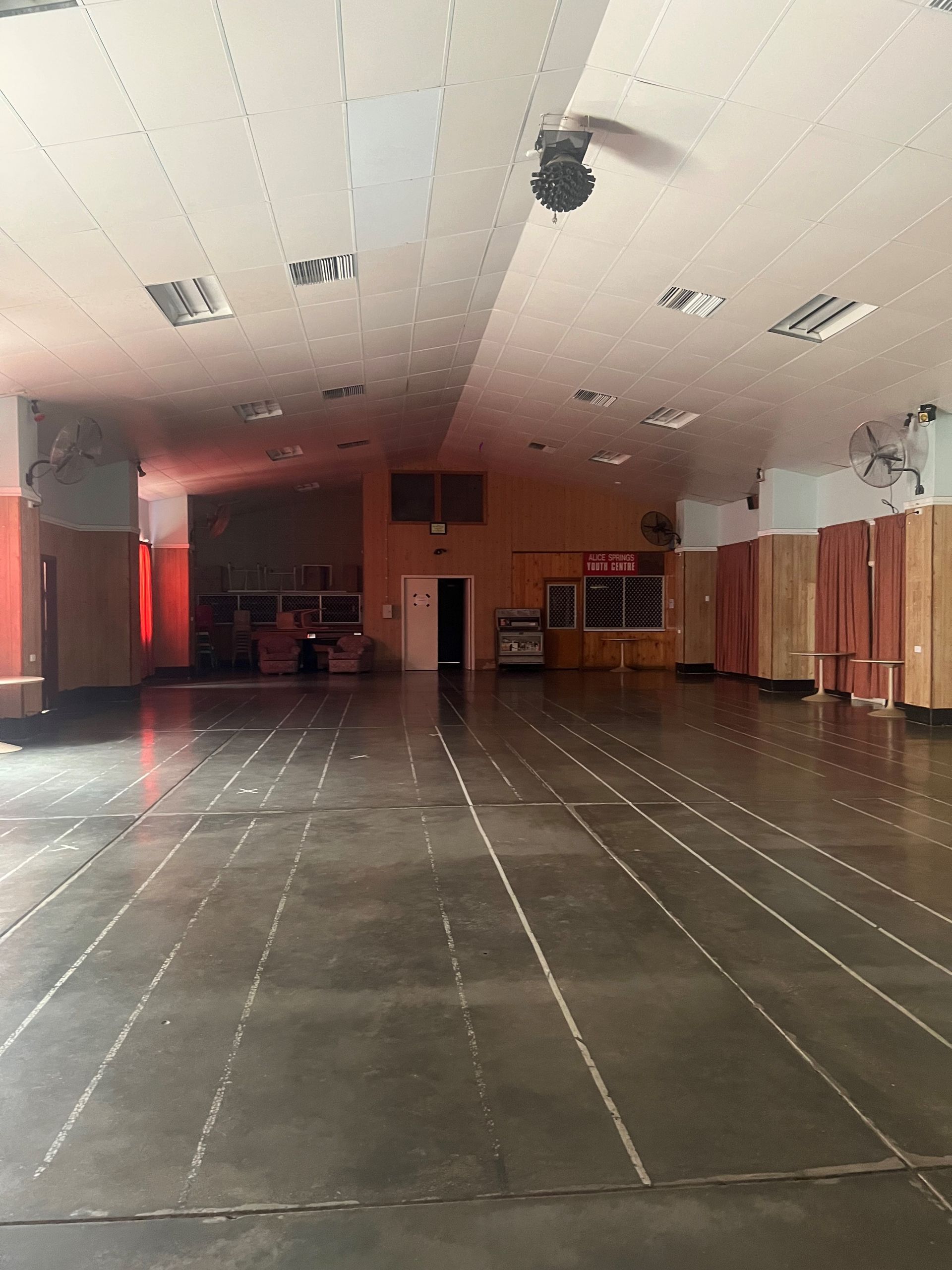 Empty, large interior space with a dark floor, white ceiling, and orange walls.
